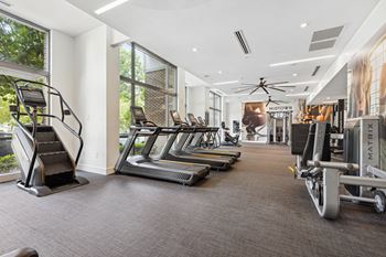 a gym with cardio equipment and large windows